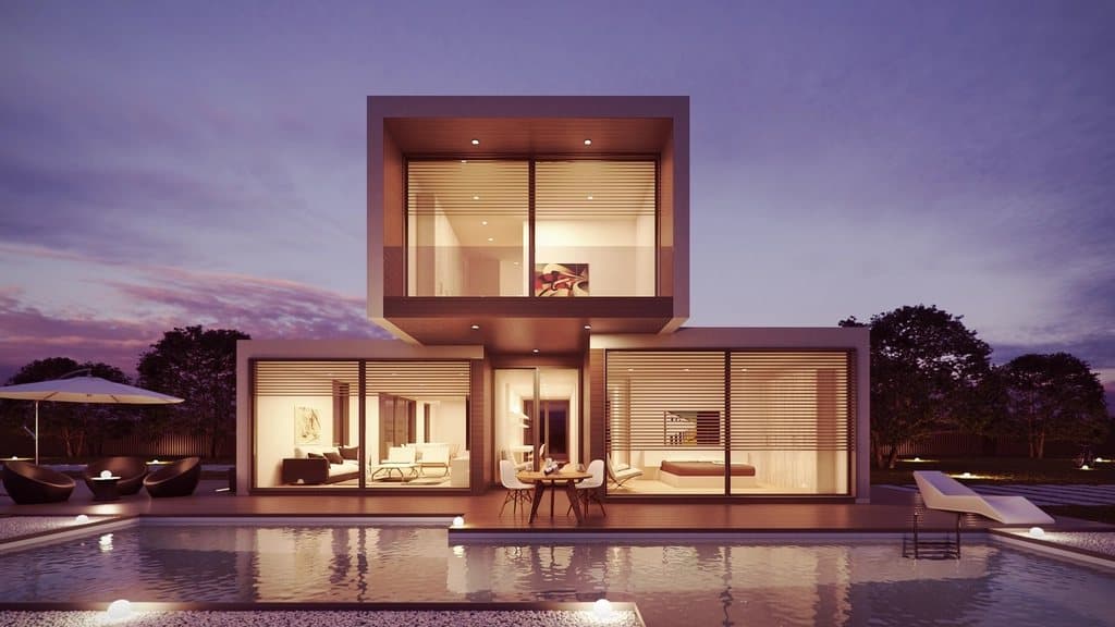 Modern two-storey villa with glass walls and a lit pool at dusk